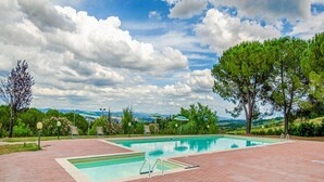 A rectangular swimming pool with a brick deck, surrounded by trees and a view of distant hills. - Montaione Harmony: Lodging (Varna - Gambassi Terme-Fi)