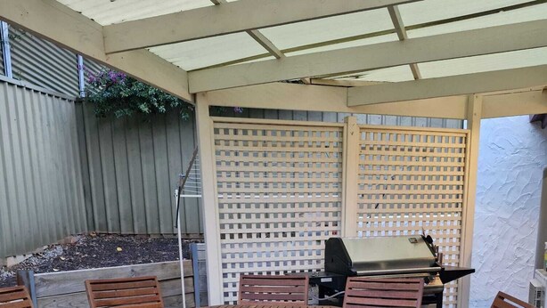 An outdoor patio with a round wooden table and chairs, a grill, and a lattice fence. - Adelaide Escape: Two-Storey Home Near City & Hills (Teringie)