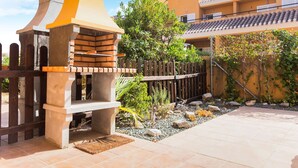 Un patio con una parrilla, una cerca de madera y un sendero empedrado.