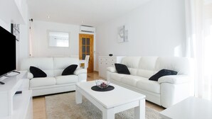 Una sala de estar moderna con dos sofás blancos, una mesa de centro blanca y un televisor de pantalla plana.