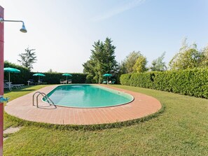 Piscina rectangular con plataforma de ladrillo, rodeada de césped verde y árboles.