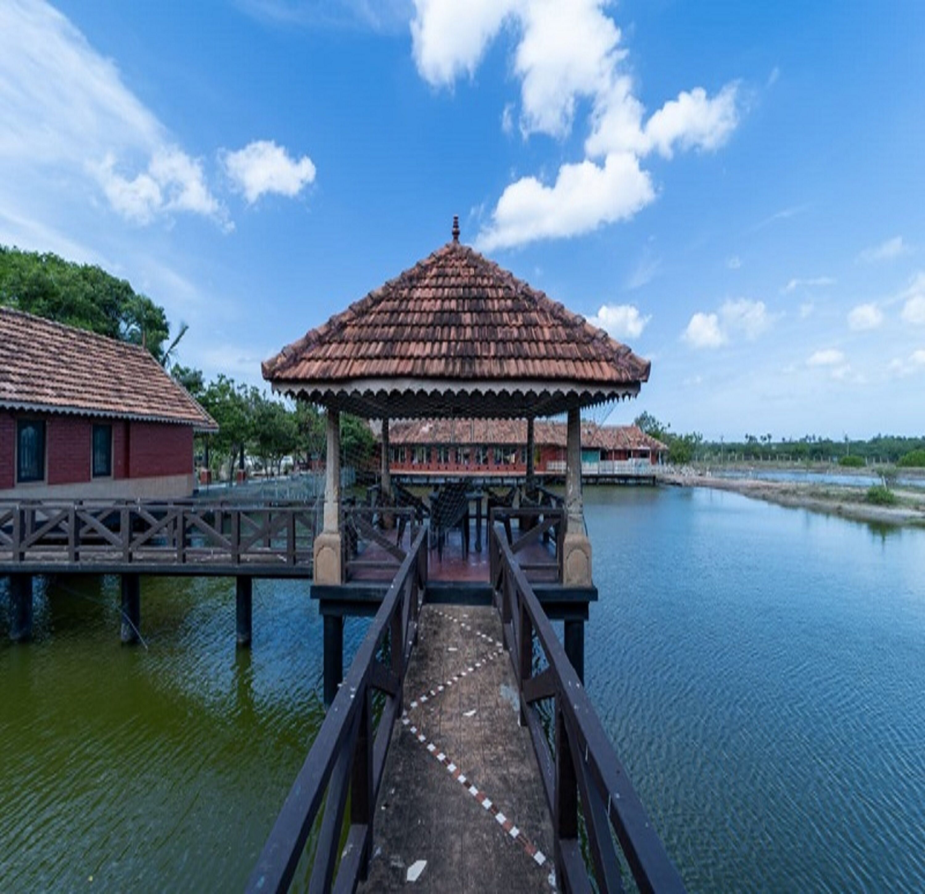 A wooden bridge leading to a gazebo with a tiled roof over a calm body of water.