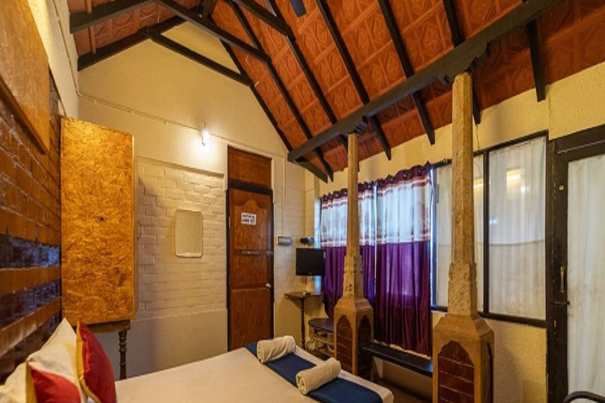 Una habitación con dos camas, una pared de ladrillo, techo de madera y una ventana con cortinas moradas.