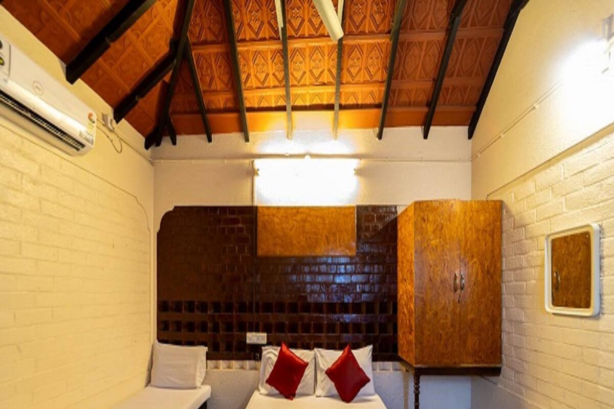 Una habitación con dos camas, techo de madera, pared de ladrillo y un mueble de madera.