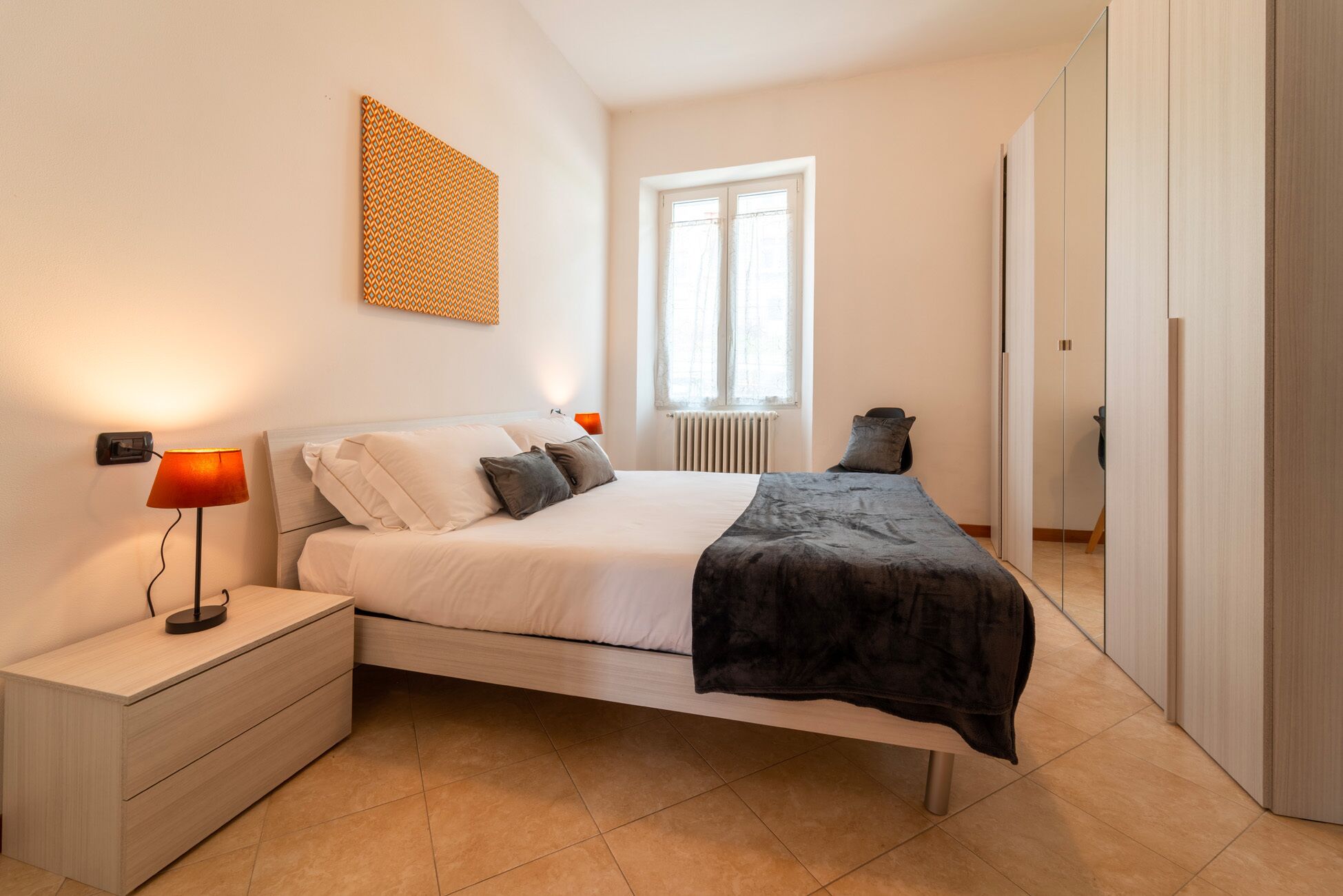 Un dormitorio con cama, mesitas de noche, lámpara, radiador y ventana.