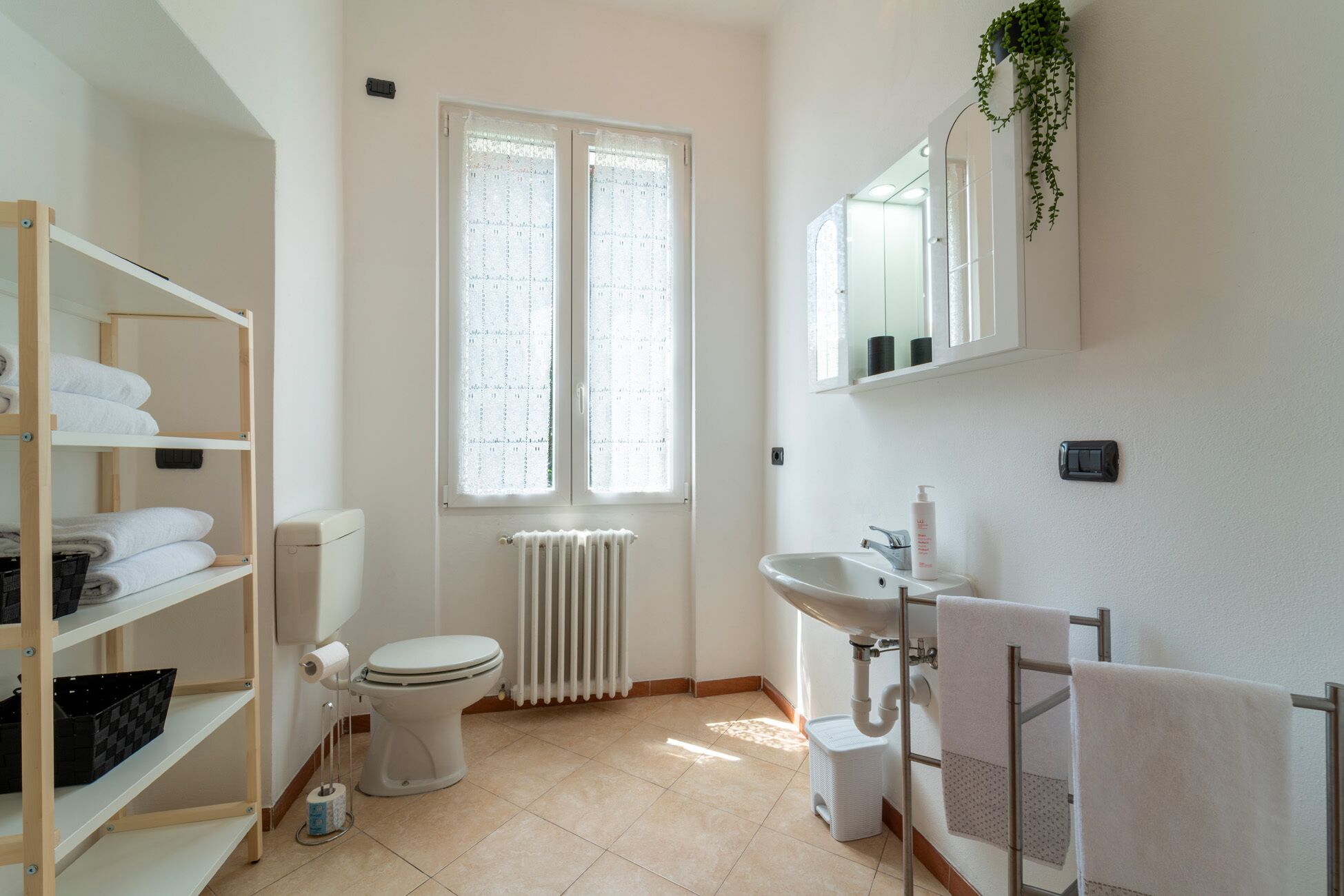 A clean, modern bathroom with a toilet, sink, and shelves for towels.