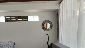 Una habitación pequeña y funcional con cama, una silla, espejo en la pared y ventana con cortinas.