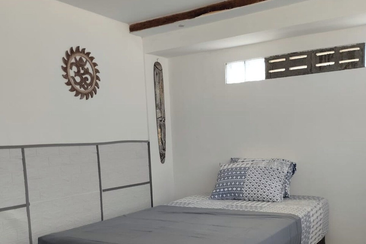 A bedroom with a bed, a headboard, a wall decoration, and a window.