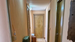 A hallway with wooden flooring, a green radiator, a small table, and a door at the end.