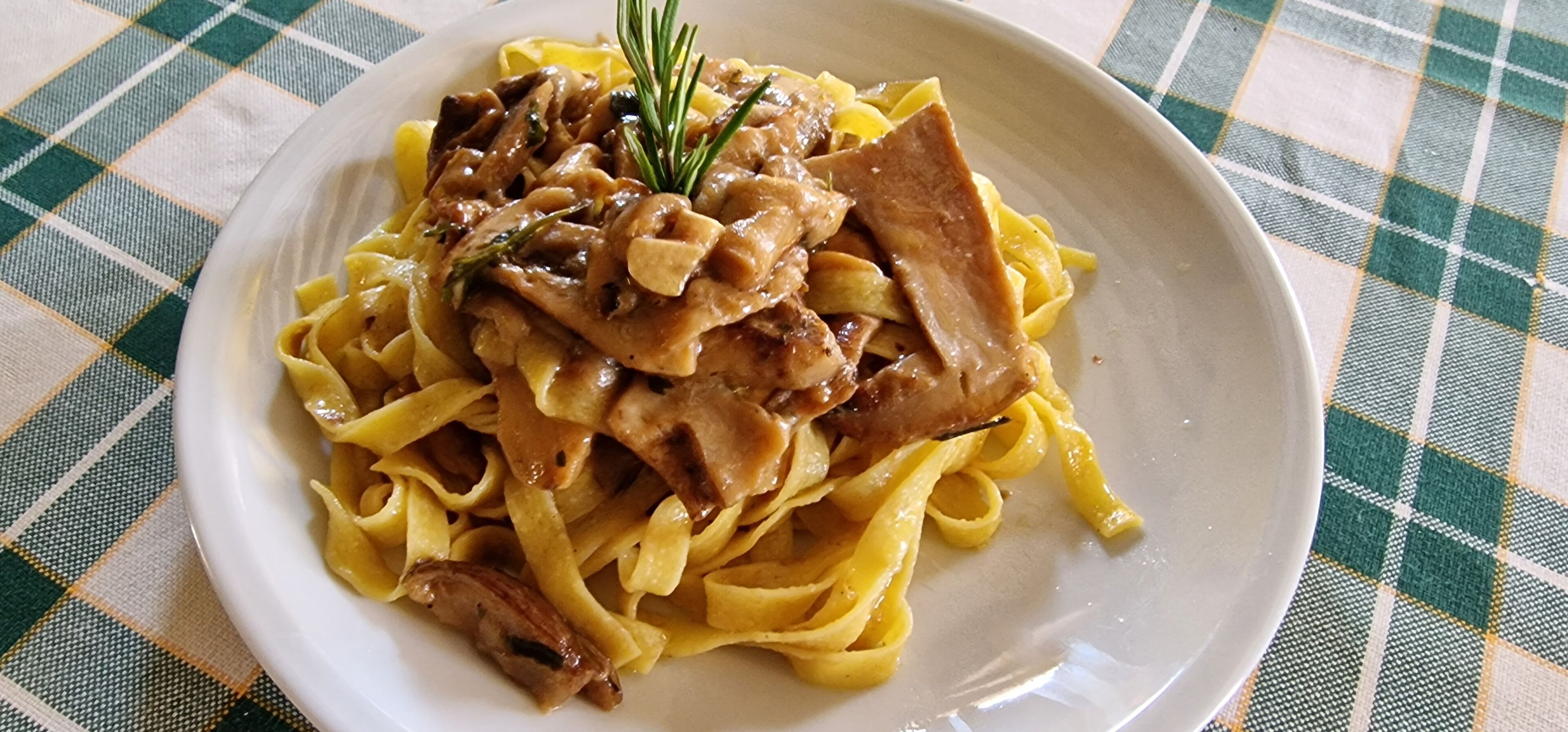 Un piatto di pasta con funghi e un rametto di rosmarino.