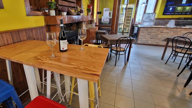 A restaurant interior with wooden tables and chairs, a wine bottle on one table, and a counter area in the background.