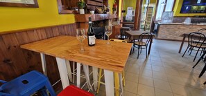 Interior de restaurante con mesas y sillas de madera, una botella de vino sobre una mesa y una barra de fondo.