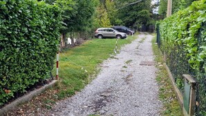 A gravel path flanked by dense green foliage, leading to a parked car.