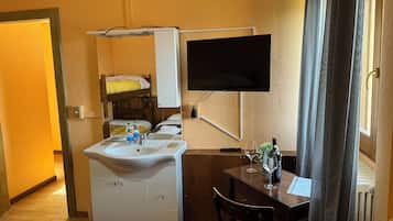A compact room with a bed, a sink, a mirror, a TV, and a small table with a chair.