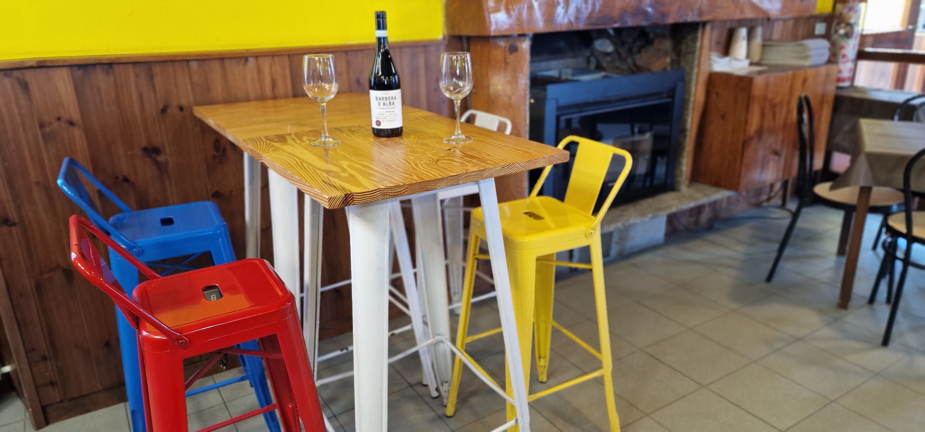 A wooden table with two wine glasses and a bottle of wine, surrounded by colorful chairs.