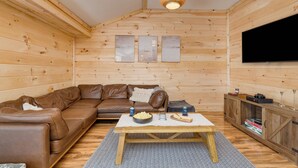 L’intérieur d’un chalet en bois chaleureux et accueillant, avec un canapé en cuir marron, une table en bois sur laquelle sont disposés des en-cas et un téléviseur fixé au mur.