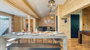 Un intérieur en bois comprenant une table à manger dressée pour un repas, une table de billard et un coin salon confortable.