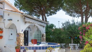 A courtyard with a stone floor, a white building with a tiled roof, and various potted plants. - La Bahia by Interhome (L'Escala)