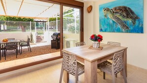 A dining area with a table and chairs, a grill outside, and a painting of a sea turtle on the wall. - Detinsa by Interhome (Sant Jordi)