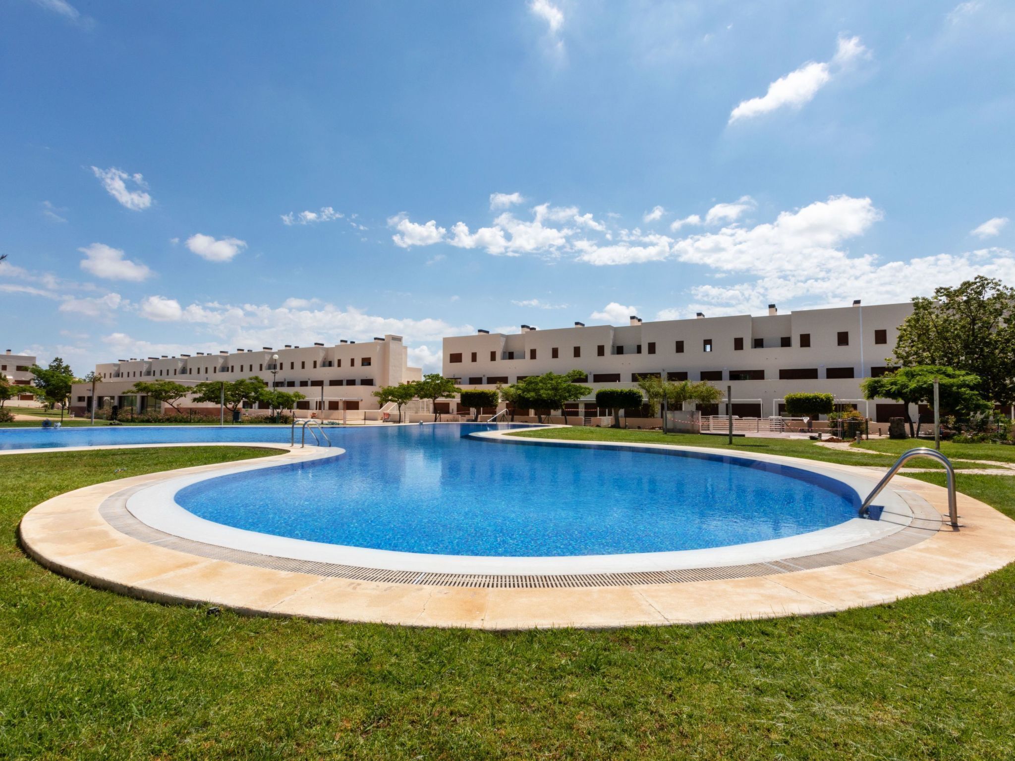 Una piscina de disseny circular, envoltada per una zona verda i un edifici al fons.