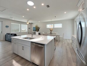 Una cocina moderna con una isla central, electrodomésticos de acero inoxidable y un comedor con mobiliario blanco.