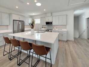 A modern kitchen with white cabinetry, stainless steel appliances, and a central island with bar stools. - Phamily Tides is a brand new 4 bedroom Pool Home Sleeps 10!!! (Navarre Beach)