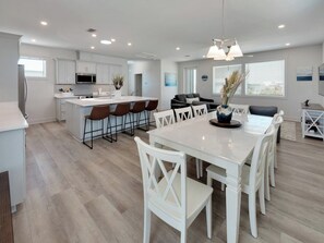 Una cocina moderna con armarios blancos, una isla central con taburetes y una zona de comedor con mesa y sillas blancas.