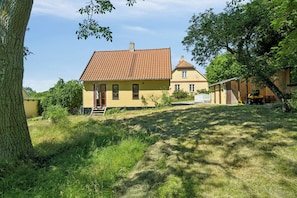 A yellow house with a red roof, surrounded by trees and a grassy yard.