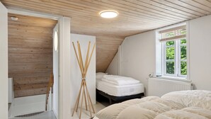 A bedroom with a sloped ceiling, a bed with white bedding, a window with blinds, and a radiator.
