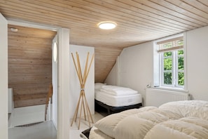 Et soveværelse med skråvæg, en seng med hvide sengetøj, et vindue med persienner og en radiator.