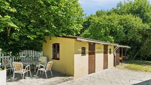 A small yellow building with a door and window, a white picket fence, and a table with chairs outside.