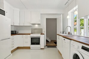 Une cuisine moderne avec des meubles blancs, un four encastré, un four à micro-ondes et un lave-linge.