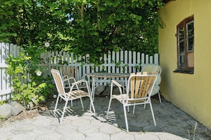 A patio with four chairs and a table, surrounded by a white picket fence and greenery.