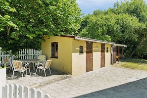A small yellow building with a door and window, a white picket fence, and a table with chairs outside. - Old local house from 1904 with natural garden (Tranekær)