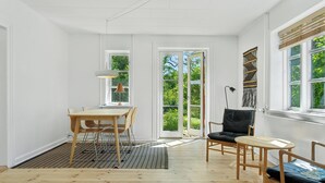 A room with a wooden floor, a dining table with chairs, a black leather chair, a small round table, and a window with a view of greenery.