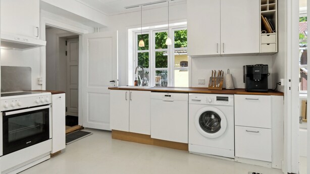 A modern kitchen with white cabinetry, a built-in oven, a washing machine, and a coffee maker.