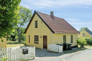 Et gult hus med brunt tag, hvid stakittet hegn og en postkasse.