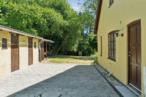 Eine schmale Kopfsteinpflasterstraße, gesäumt von Gebäuden mit Holztüren und -fenstern, die zu einer grünen Parkanlage führt.