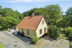 Ein eingeschossiges Haus mit rotem Ziegeldach, Schornstein und einer kleinen Veranda mit weißem Zaun.