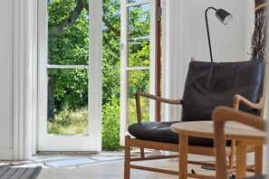 Une pièce avec une chaise en bois, un lampadaire et une grande fenêtre donnant sur un paysage verdoyant.