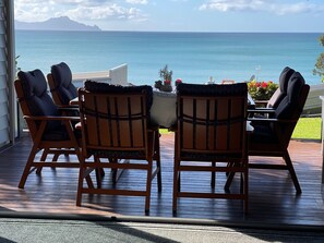 A wooden deck with four chairs and a table, overlooking a body of water and a distant mountain. - Langs Beach Luxury Apartment (Langs Beach)
