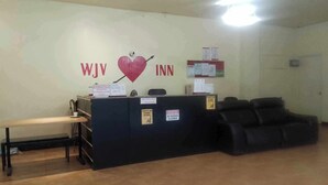 Uma mesa de recepção com um símbolo de coração e o texto "WJV INN" na parede. Há placas indicando que não há trocas, sem política de cancelamento e proibido porte de chave ou saída.