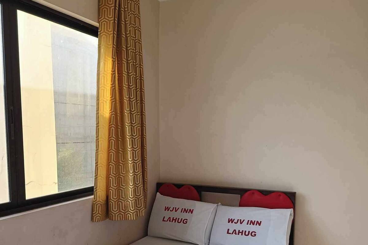 A single bed with two pillows labeled "WJV INN LAHUG" and a pair of rolled towels with a green bow.