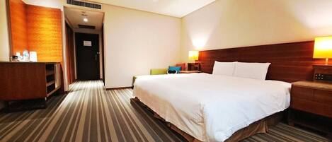 Habitación de hotel con una cama grande, una mesita de noche, un escritorio, una silla y una puerta que da a otra habitación.