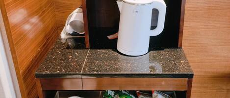 Minibar de una habitación de hotel con cafetera, botellas de agua, vasos y sobres de té.
