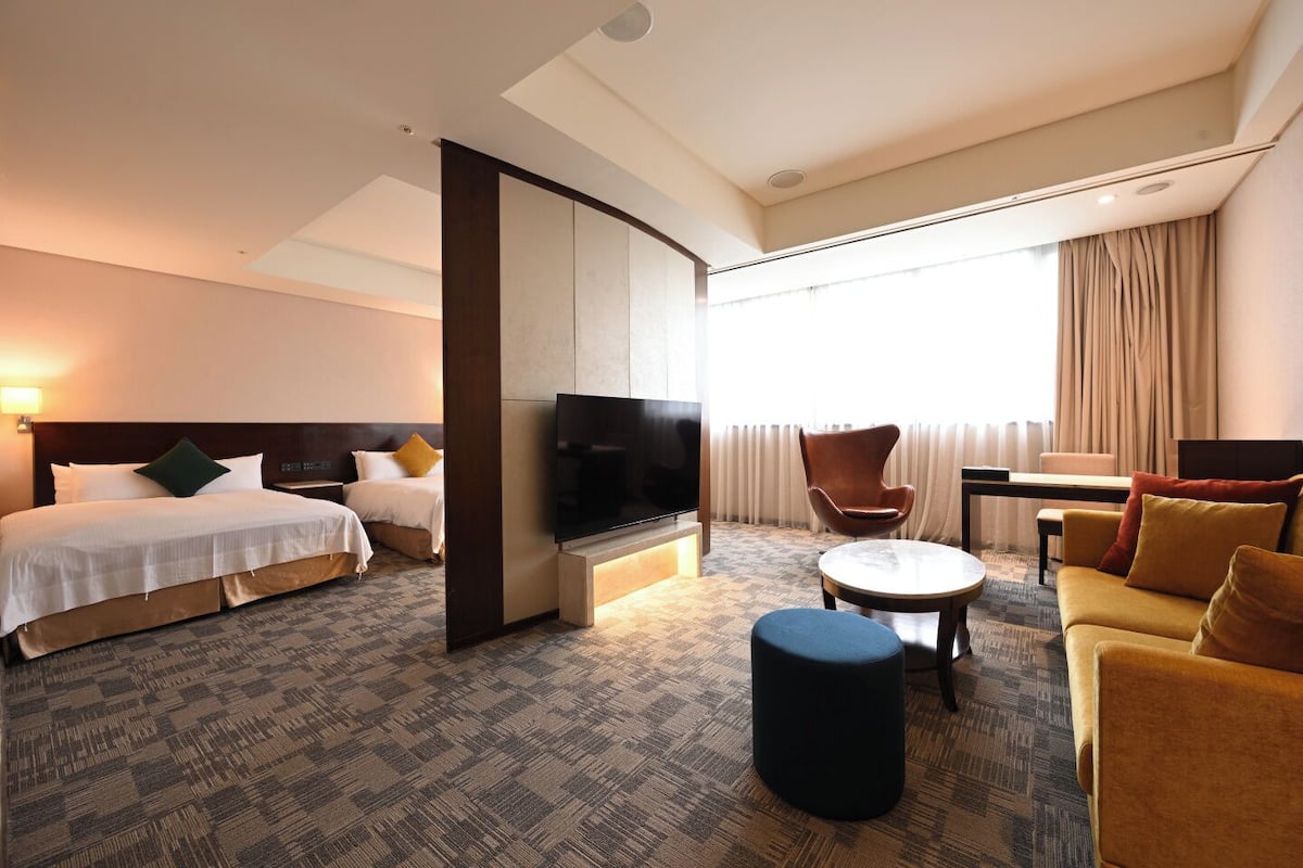 A hotel room with a bed, a TV, a sofa, a chair, and a small table.