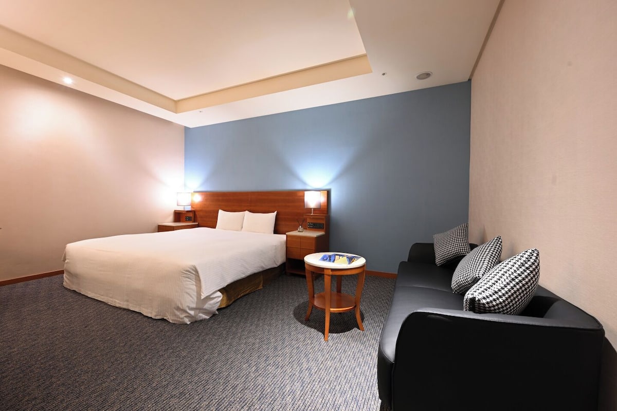 A hotel room with a bed, a small table, a sofa, and a nightstand.