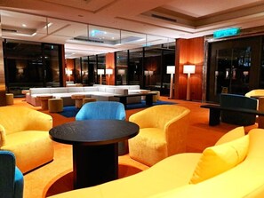 A modern lobby with a seating area featuring sofas and armchairs, a coffee table, and a large window providing a view of the cityscape. - Via Hotel Breeze (New Taipei City)