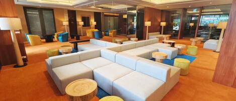 A modern hotel lobby with a sectional sofa, round wooden tables, and a carpeted floor.