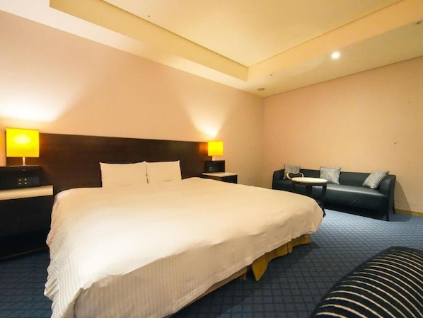 Une chambre d’hôtel avec un grand lit, deux tables de chevet avec des lampes, un canapé en cuir noir et une petite table ronde.